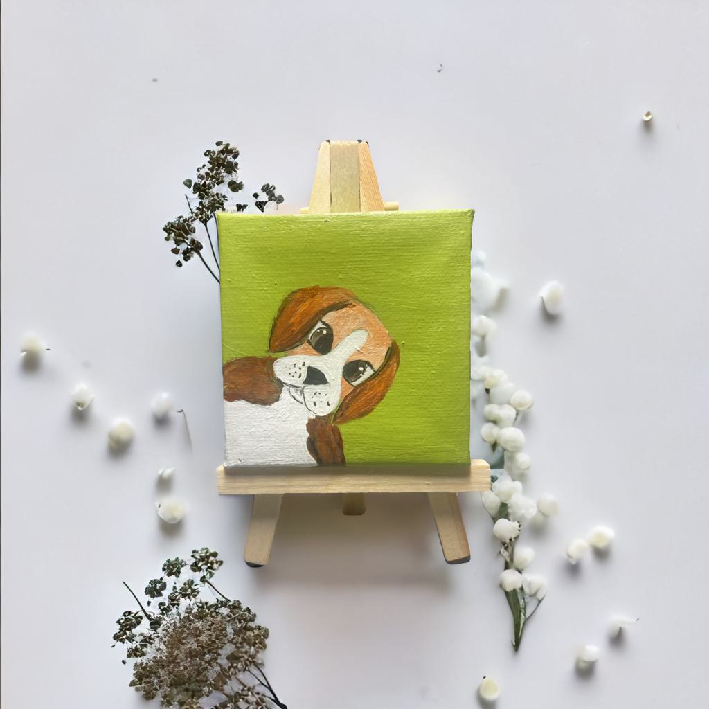 Mini Leinwand 7x7 cm mit handgemaltem Hund auf grünem Hintergrund, auf kleiner Holzstaffelei mit Trockenblumen dekoriert.