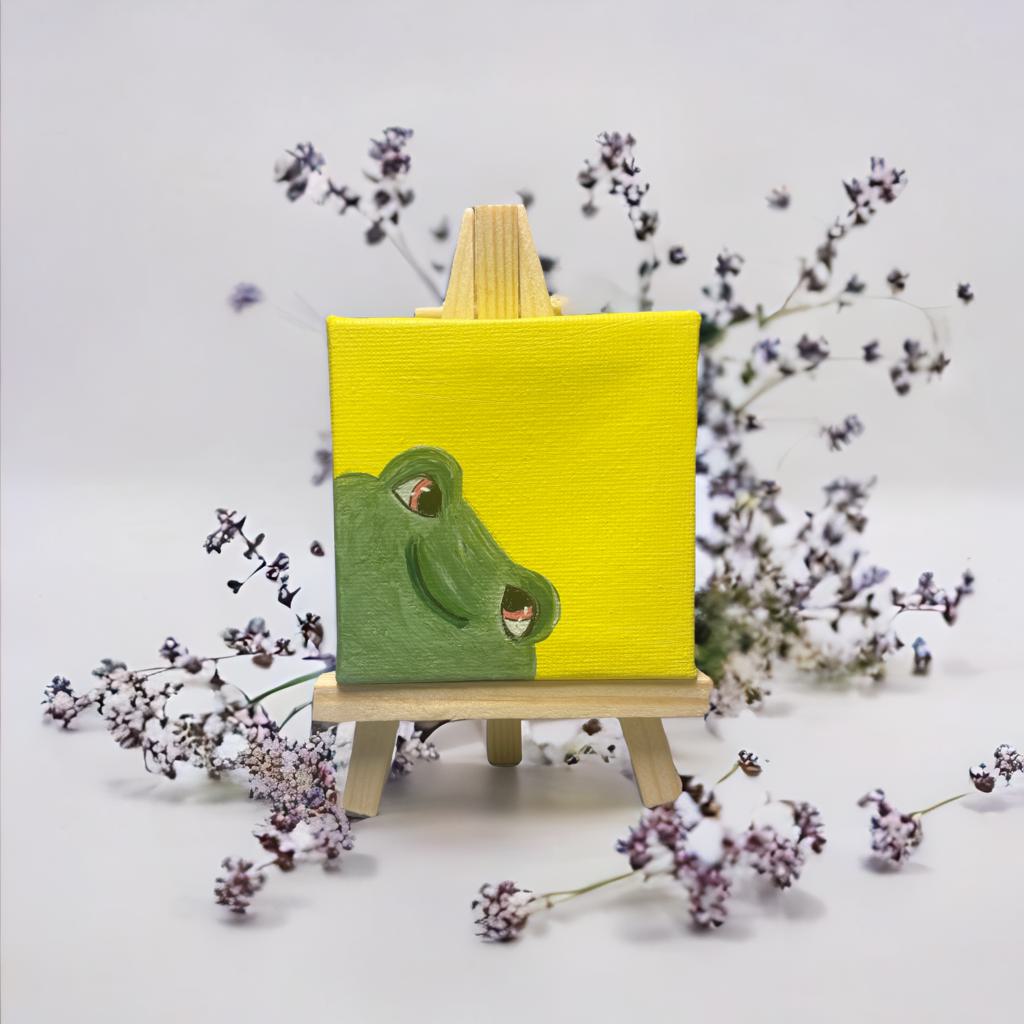 Mini Leinwand 7x7 cm mit handgemaltem Frosch auf leuchtend gelbem Hintergrund, auf Holzstaffelei dekoriert mit lila Trockenblumen – farbenfrohe Dekoidee.