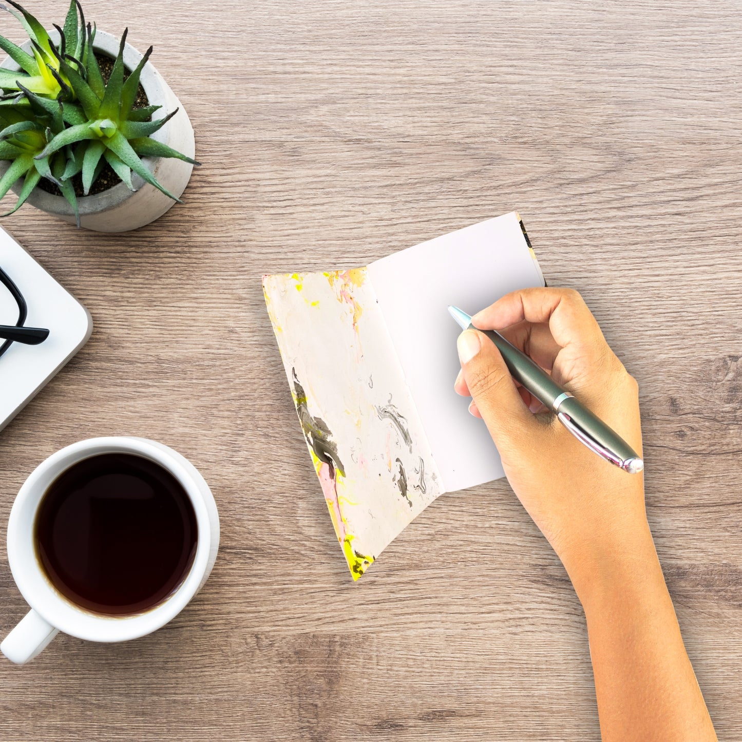 Szene mit Seluna aufgeklappt, während eine Hand hineinschreibt – Kaffeetasse und Pflanze im Bild.