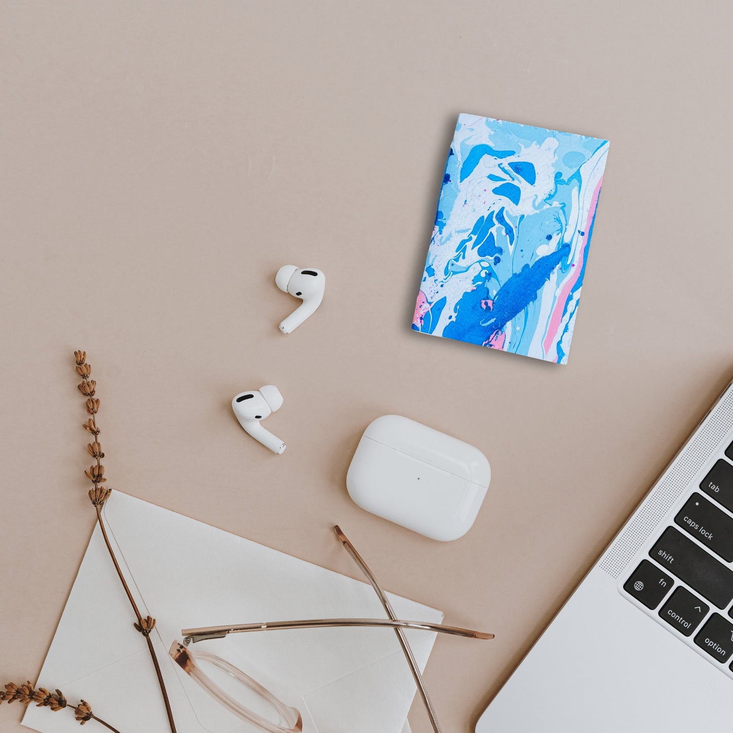  Aven Notizbuch mit blau-weiß-pinker Marmoroptik, arrangiert neben AirPods, Laptop und Brille auf einem modernen Arbeitsplatz.