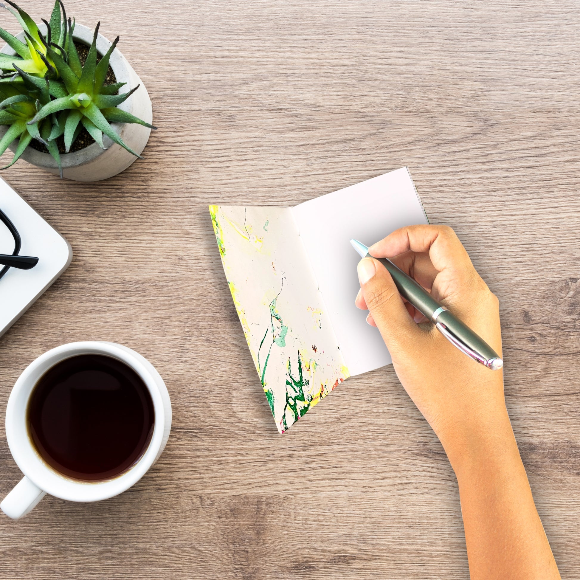 Geöffnetes Evora Notizbuch mit individueller Marmorierung auf einem Holztisch, daneben eine Tasse Kaffee – ideal für Skizzen oder Gedanken.

