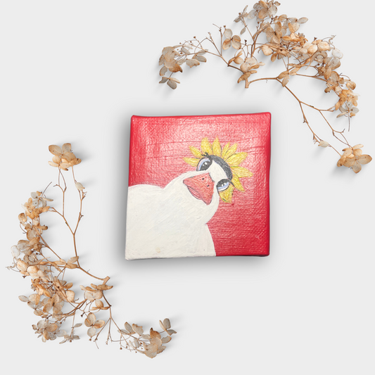 Handgemalte Mini Leinwand 7x7 cm mit weißer Ente im Sonnenblumenhut auf rotem Hintergrund, liebevoll dekoriert mit Trockenblumen – humorvolle Deko mit Herz.