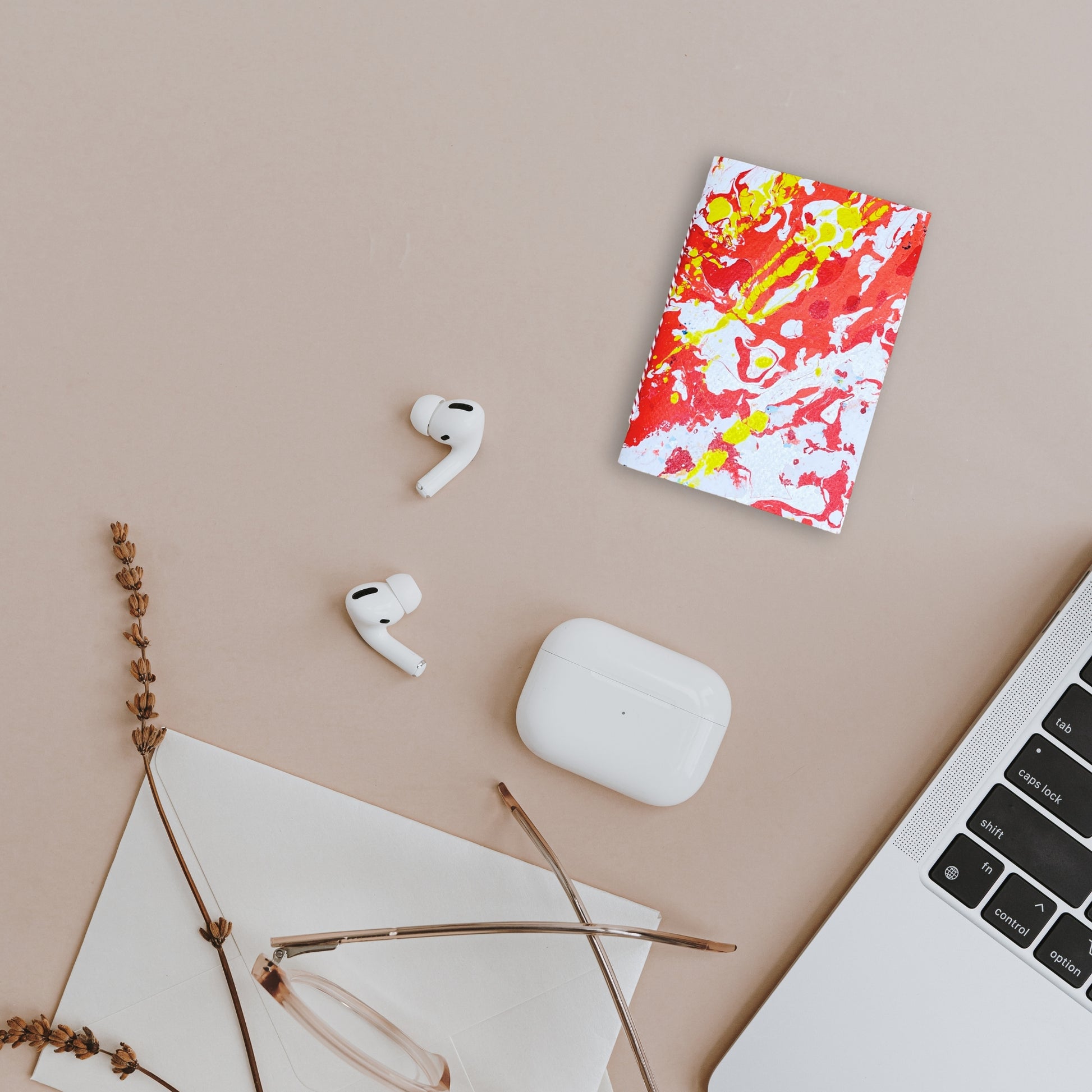 Szenische Darstellung mit Notizbuch Oris, AirPods, Laptop und getrockneten Zweigen.